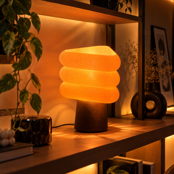 Kiro Aurelle sculptural table lamp with three rounded triangular beige layers, a tapered brown base and warm yellow illumination.